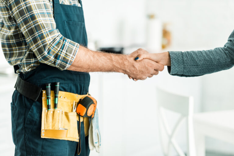 cropped image of plumber and client shaking hands in kitchen