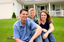 two smiling parents with their son in their front yard