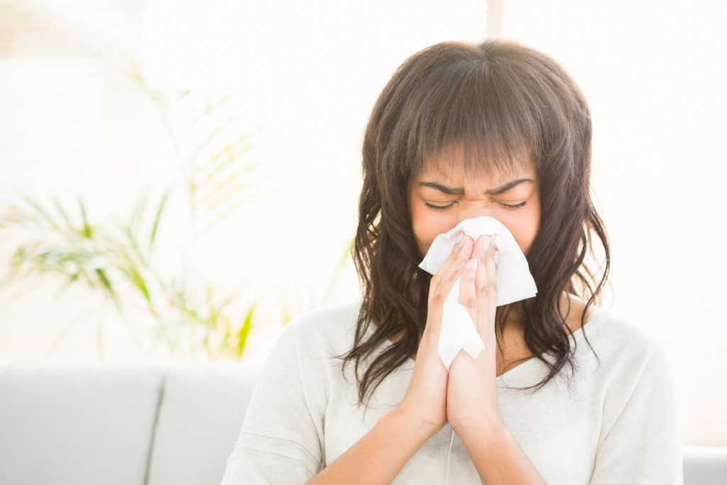 Woman sneezing on couch at home in living room