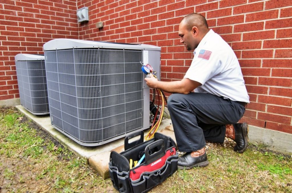 ABC technician kneeling by outside unit providing residential AC tune-up services