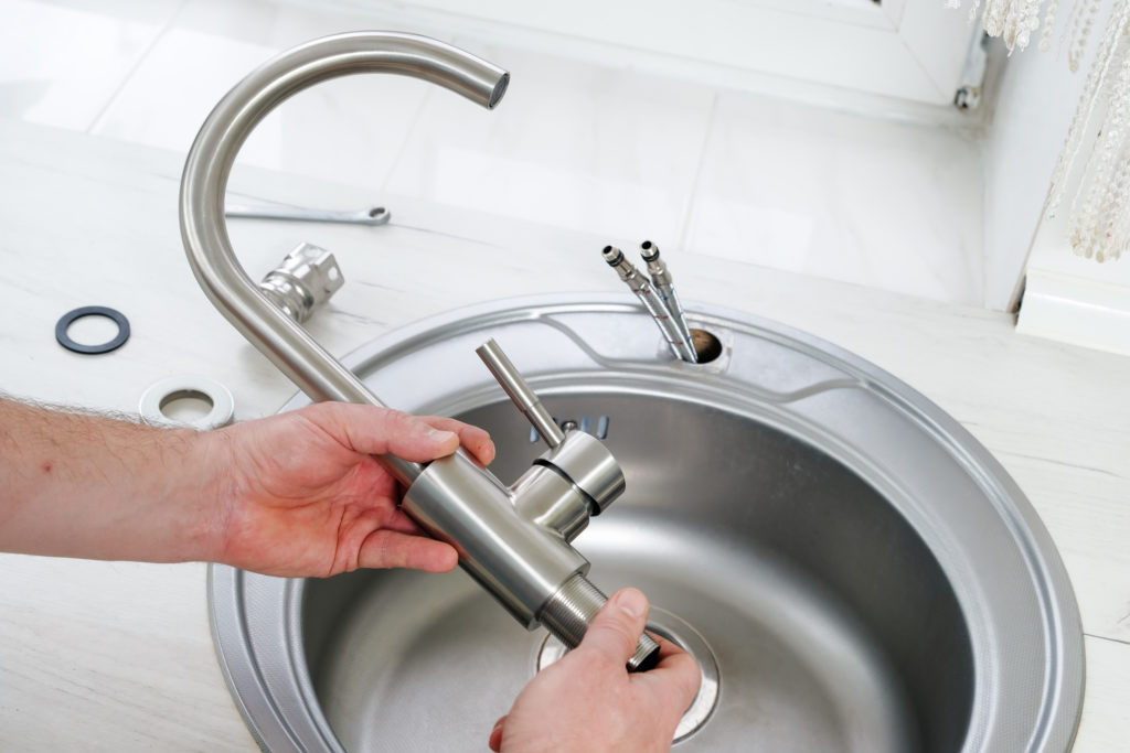 Plumber hand holds a new faucet for installing into the kitchen sink
