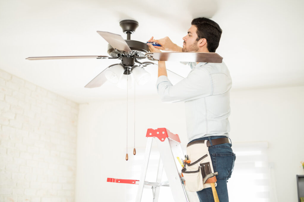 handyman stepping on a ladder and installing a ceiling fan